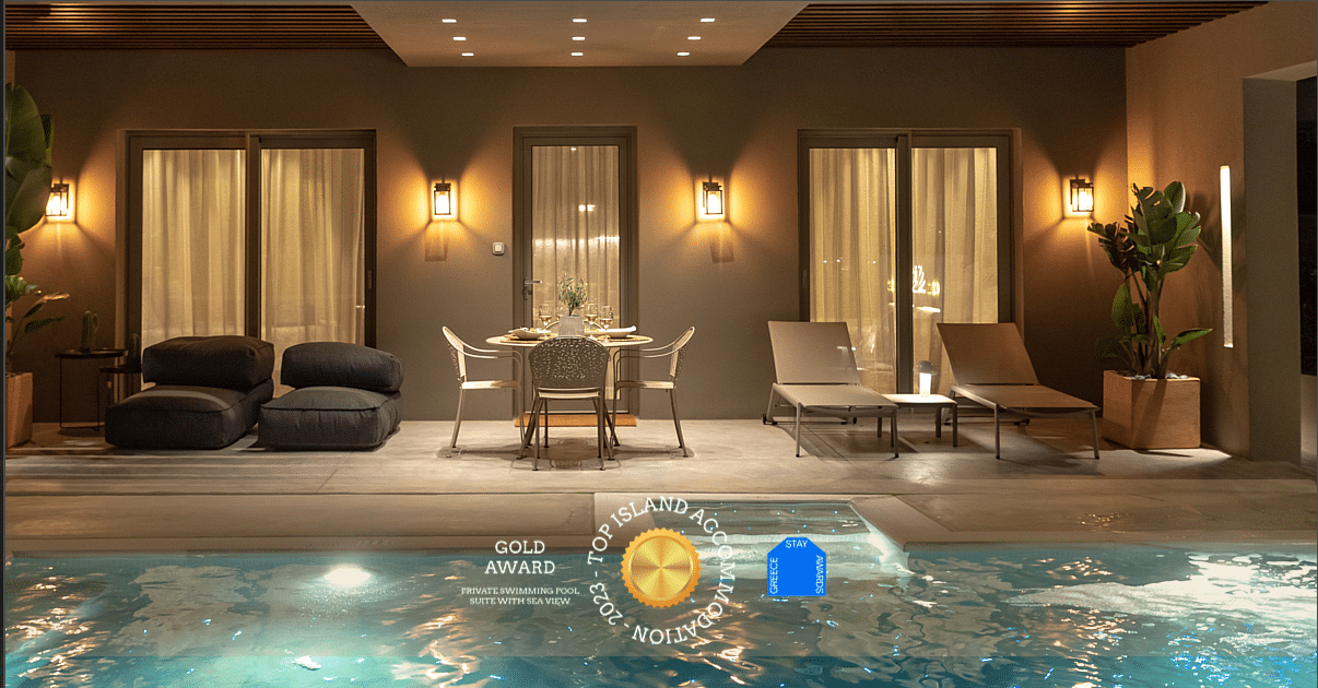 Dreamy photo of a private swimming pool villa complex at night, fully illuminated, with a gold award logo "Top Island Accommodation 2023 - Greece Stay Awards"